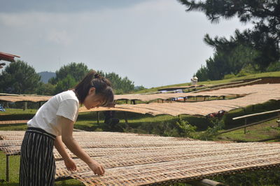 Woman adjusting wickers over field against sky