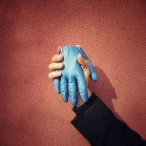 Cropped hand of person holding glove against wall