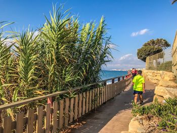 Rear view of people on walkway by sea against sky