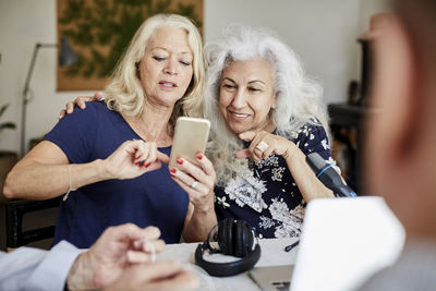 Senior woman showing mobile phone to friend while vlogging at home