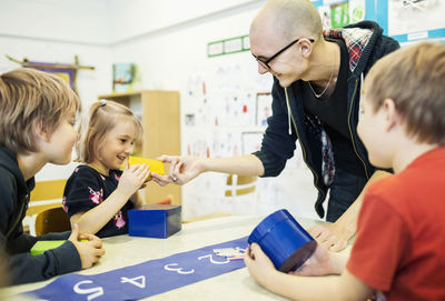 Happy teacher assisting students in art class at kindergarten