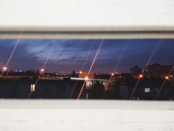 Illuminated city against sky seen through glass window