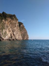 Rock formation in sea against clear blue sky