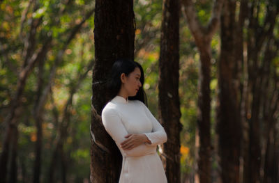 Side view of woman standing by tree trunk in forest