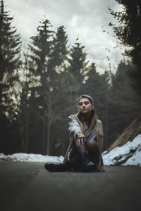 Portrait of young woman sitting in forest during winter