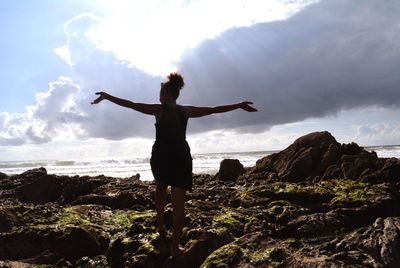 Woman standing on rock by sea against sky