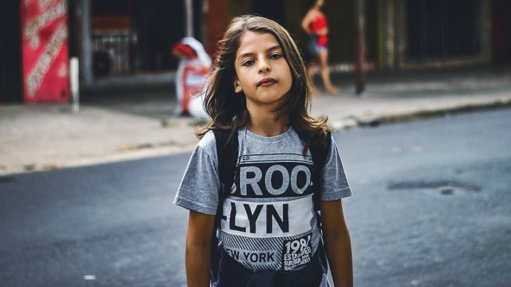 one person, front view, portrait, casual clothing, city, child, street, childhood, girls, looking at camera, standing, road, lifestyles, focus on foreground, text, day, hairstyle, leisure activity, outdoors, teenager, innocence