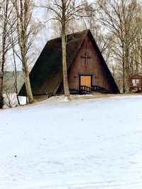 Bare trees on snow covered field by house