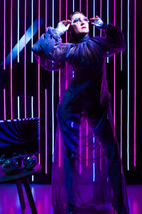 An extravagant girl poses in full height against the background of neon lights in the studio