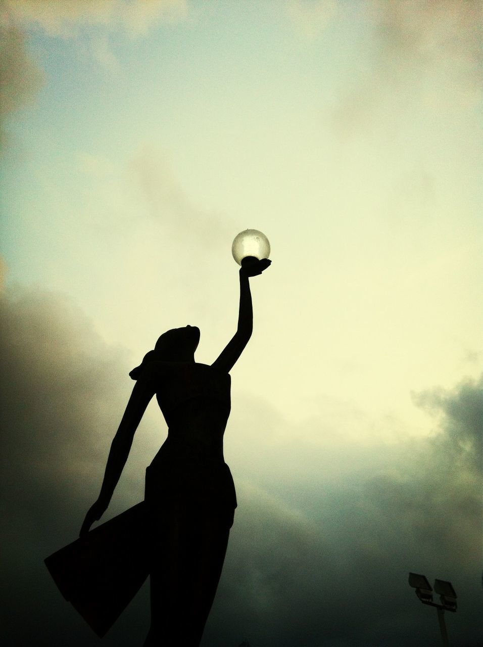 sky, low angle view, cloud - sky, one person, silhouette, cloud, cloudy, human representation, sculpture, outdoors, dusk, statue, art and craft, part of, holding, street light, day, creativity, person