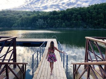 Rear view of woman in colorful summer dress walking down a wooden pontoon towards a lake