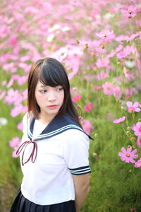 Beautiful woman looking away standing by pink flowering plants