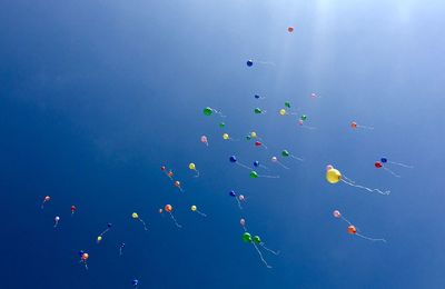 Low angle view of balloons flying in sky during sunny day