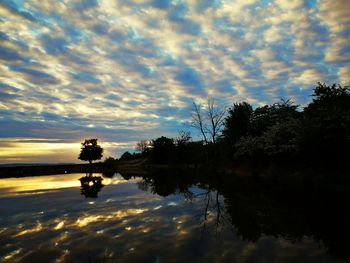 Silhouette trees by lake against sky during sunset