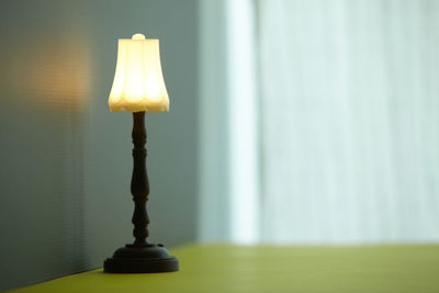 Close-up of illuminated lamp on table against wall