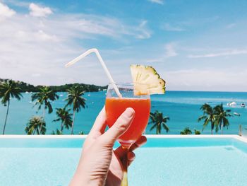 Cropped image of hand holding drink against swimming pool