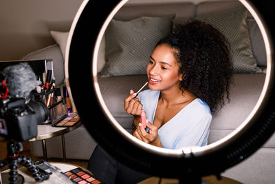 Young woman applying make-up reflecting on mirror at home