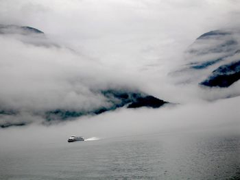 Cruise ship sailing by sea against mountains covered with clouds