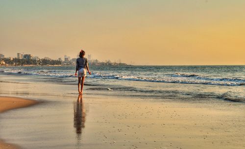 Man walking on beach against sky during sunset