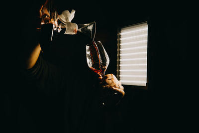 Midsection of woman holding wineglass in darkroom