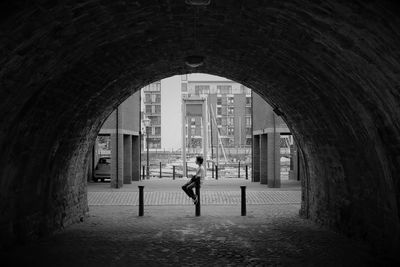 Boy sitting on bollard seen through arch