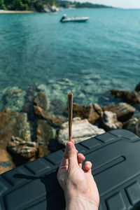 Cropped hand holding marijuana joint against sea