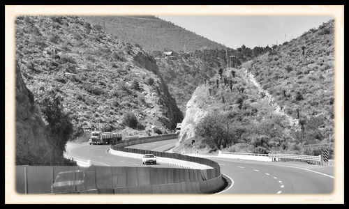 Vehicles on road by mountain against clear sky