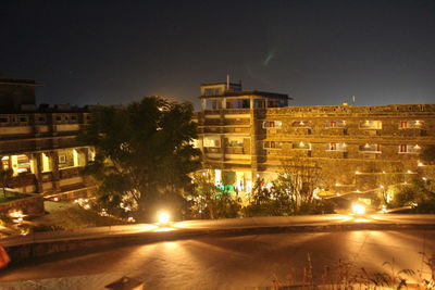 Illuminated buildings by street against sky at night