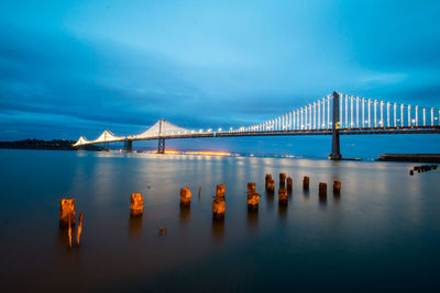 View of suspension bridge over river against cloudy sky