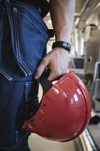 Midsection of auto mechanic teacher holding red hardhat at workshop