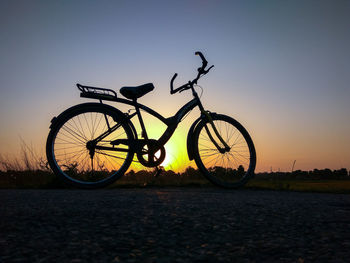 Bicycle parked on road against sky during sunset