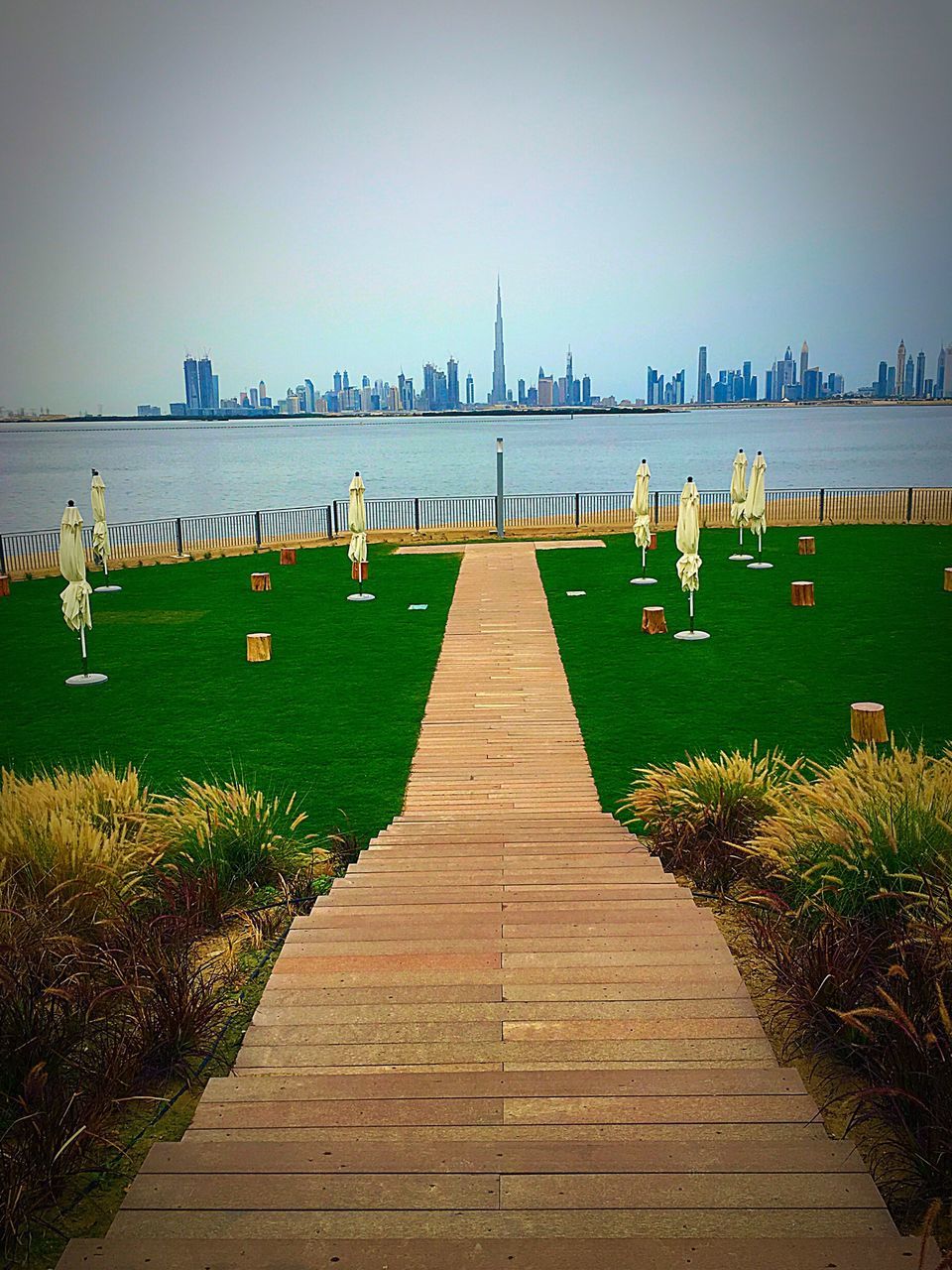 built structure, architecture, clear sky, the way forward, grass, copy space, railing, walkway, pathway, footpath, in a row, water, diminishing perspective, tranquility, building exterior, day, plant, nature, outdoors, tranquil scene