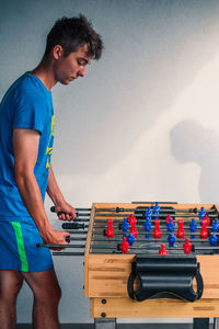 Side view of teenage boy playing foosball against wall at home