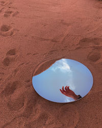 High angle view of hand and sky reflecttion and mirror and sand