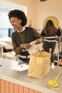 Smiling female worker with paper bag on counter at recycling center