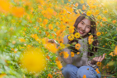 Portrait of woman crouching on land by yellow flowering plants