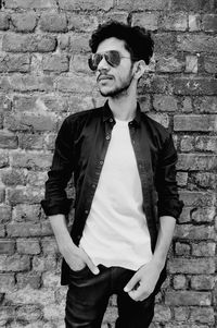 Young man wearing sunglasses looking away standing against wall