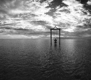 Person swinging in sea against cloudy sky