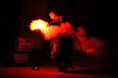 Mid adult man holding distress flare while standing on road against sky at night