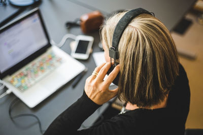 Businesswoman listening through headphones while using laptop at desk in office