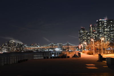 Illuminated buildings by river against sky at night in new york city.