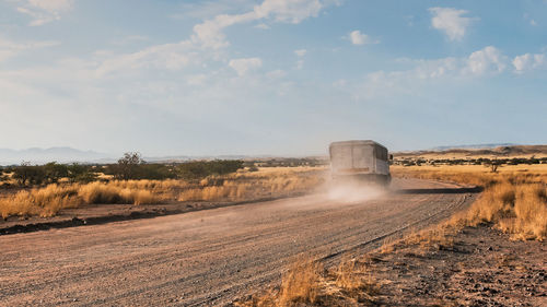 Truck blowing dust on dirt road against sky