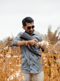 Young man wearing sunglasses standing on field against sky