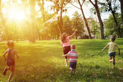 Full length of children running while flying kite on field