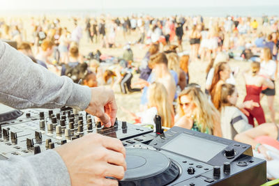 Cropped hands of dj mixing music against crowd at beach