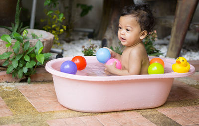 Shirtless baby boy playing with colorful balls in bathtub