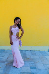 Full length of fashionable young woman standing against yellow wall