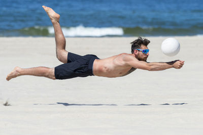 Shirtless man playing volleyball at beach