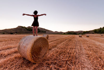 Caucasian 30s brunette woman, standing on an hay bale with arms raised