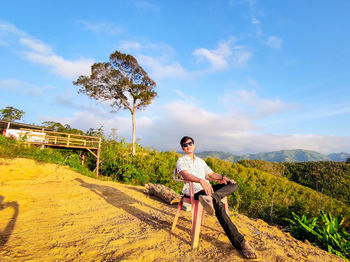 Full length of young man sitting on land against sky